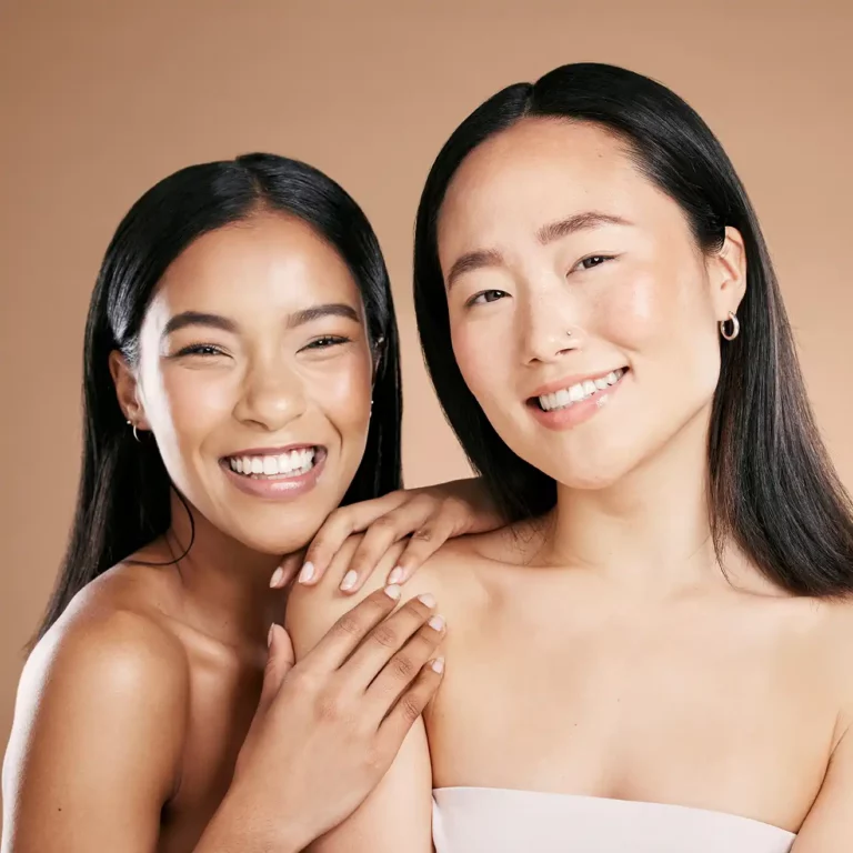 Zwei junge Frauen mit reiner Haut stehen beisammen und strahlen Lebensfreude aus